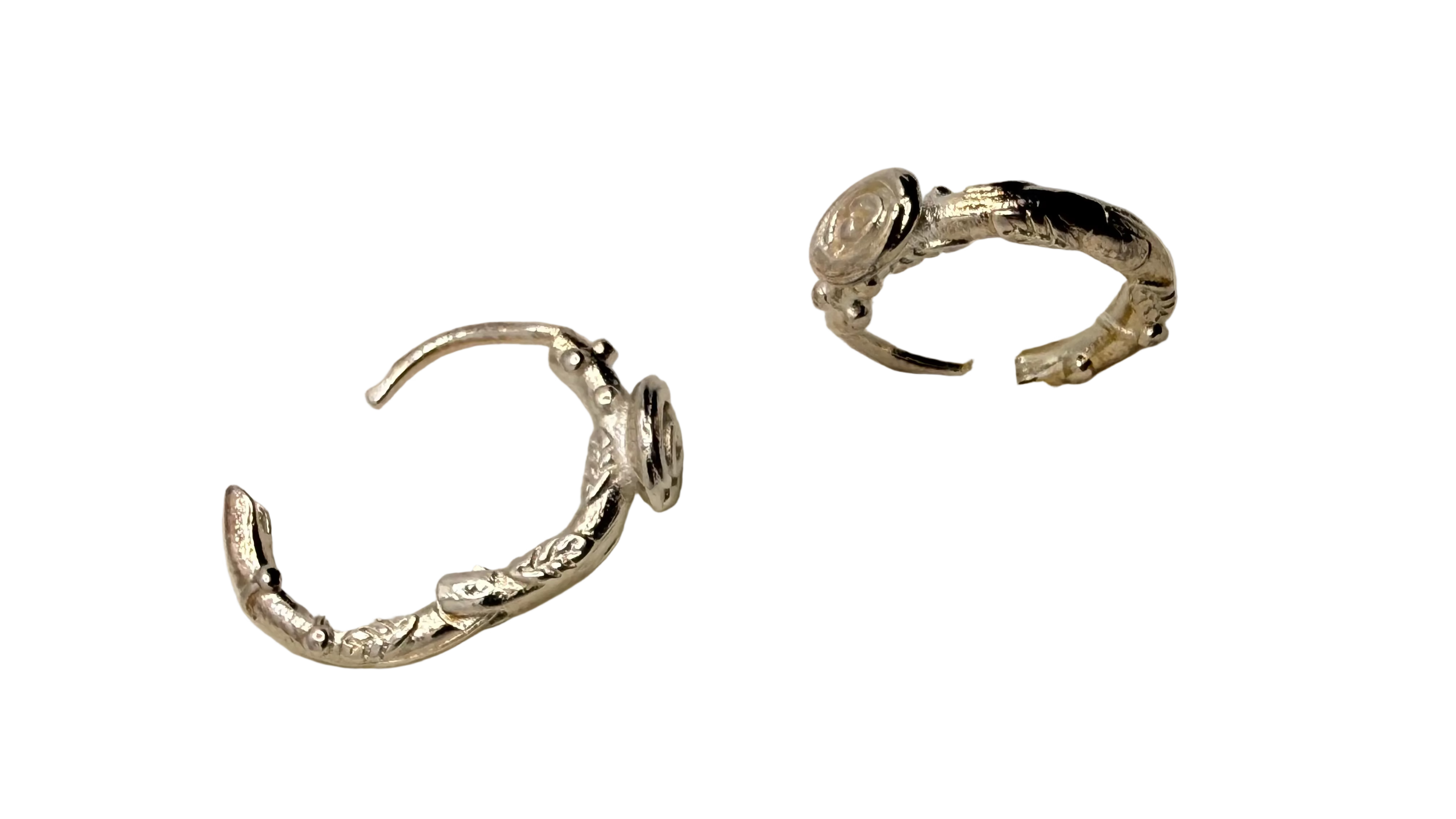 A pair of textured silver ear cuffs displayed on a white foam stand against a white background.