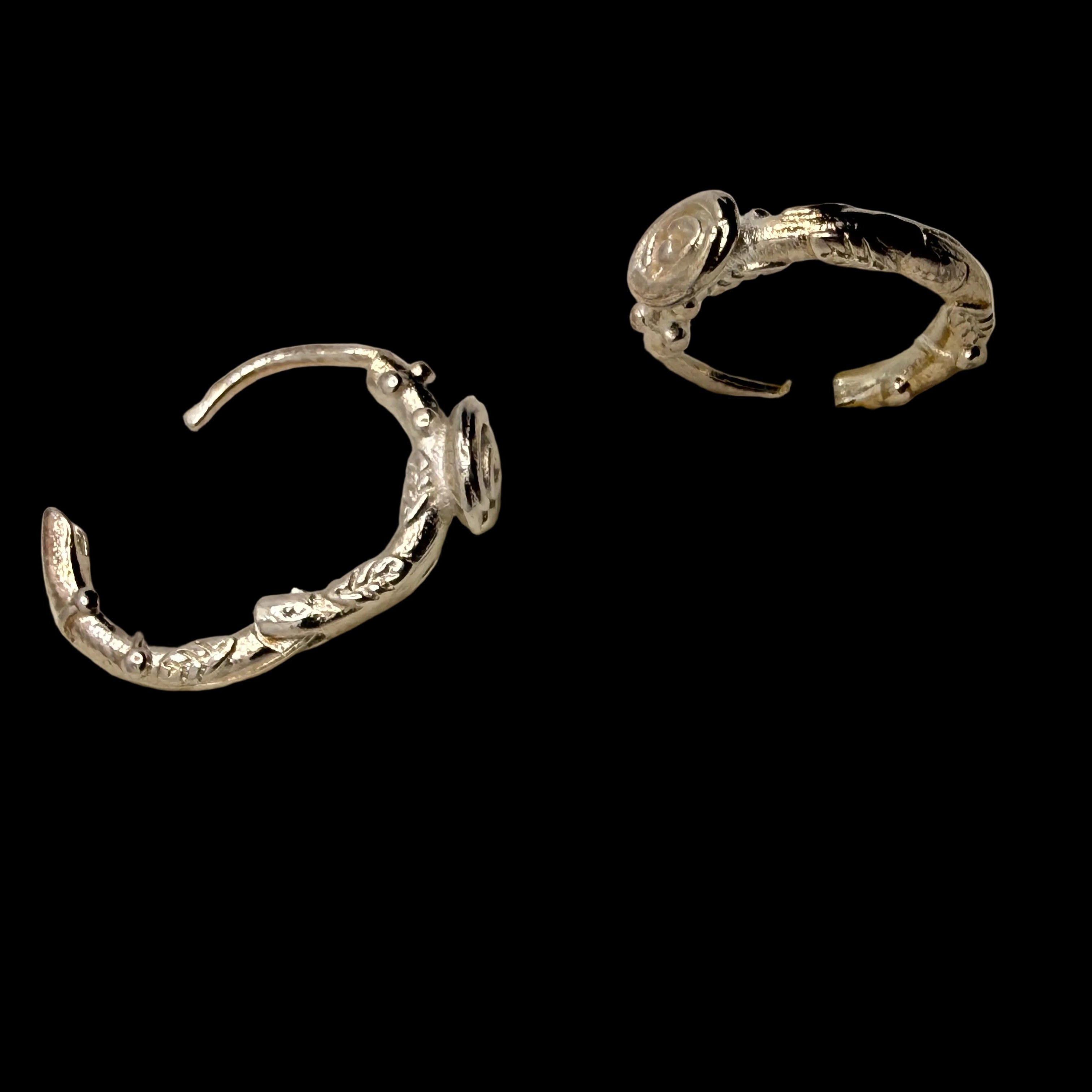 A pair of textured sterling silver huggie rings displayed on a white foam jewelry stand.