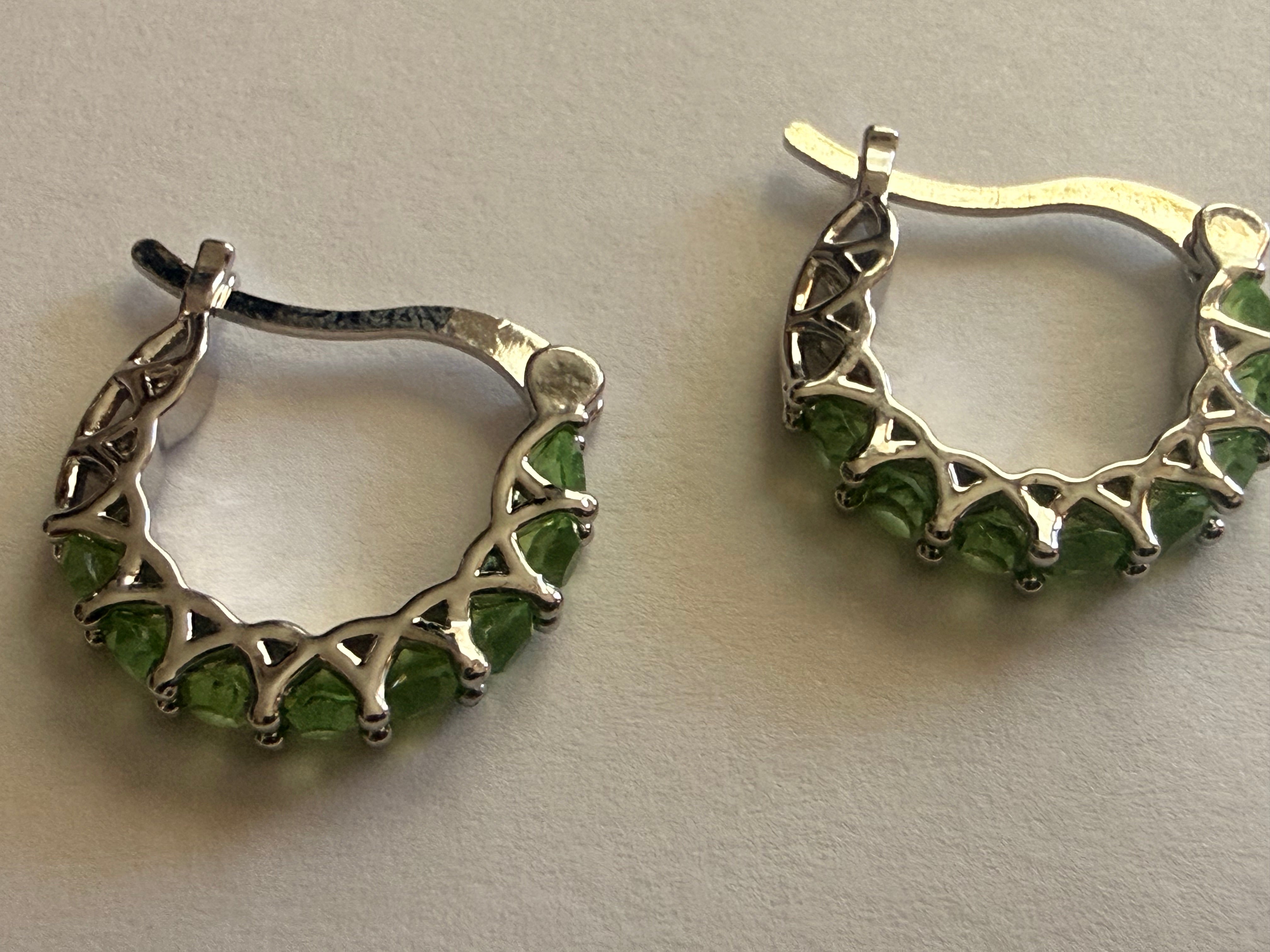 Silver-tone hoop earrings set with a row of round green rhinestones in prong settings, openwork triangular gallery, latch-back closure