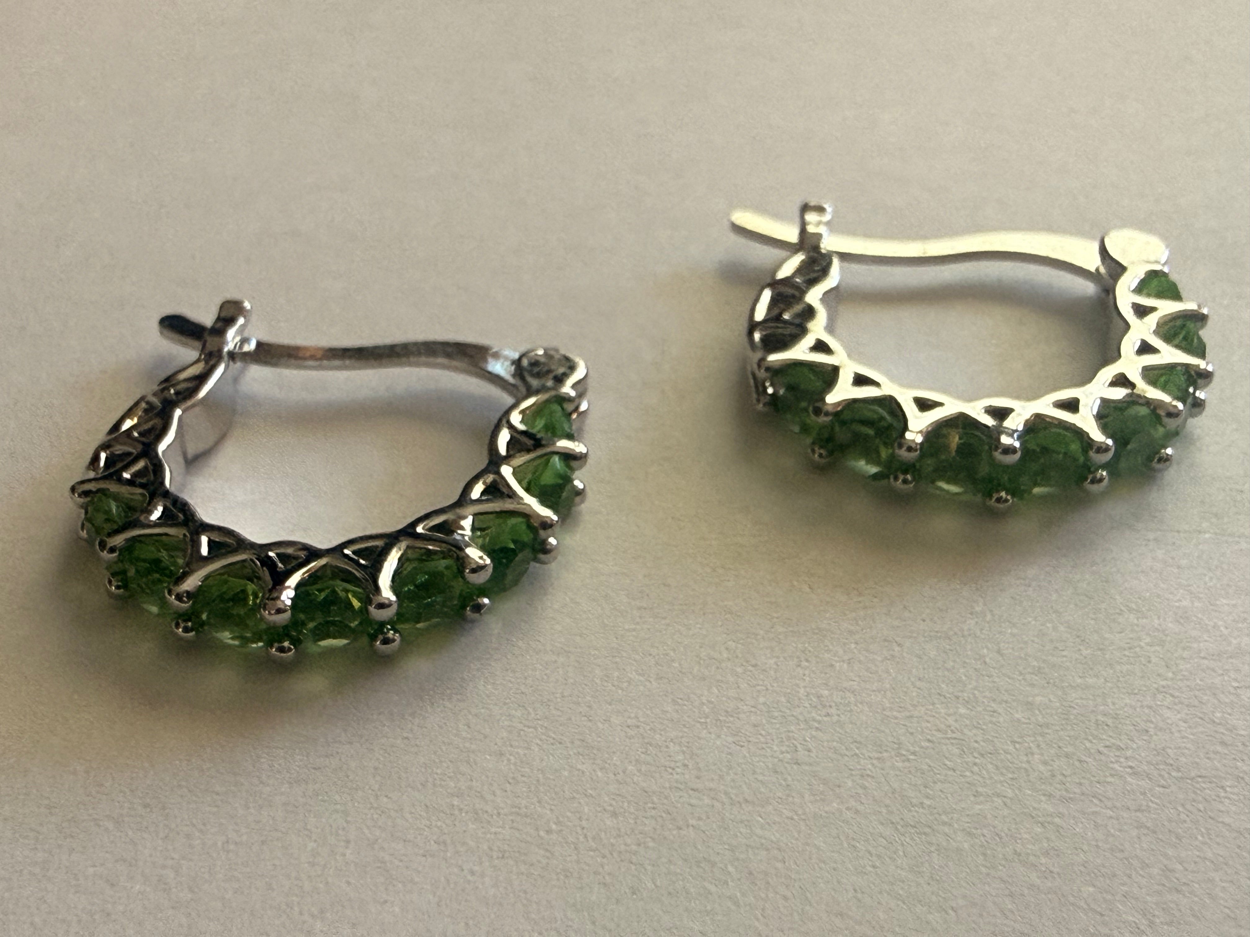 Silver-tone hoop earrings set with a row of round green rhinestones in prong settings, openwork triangular gallery, latch-back closure, pair shown front and reverse