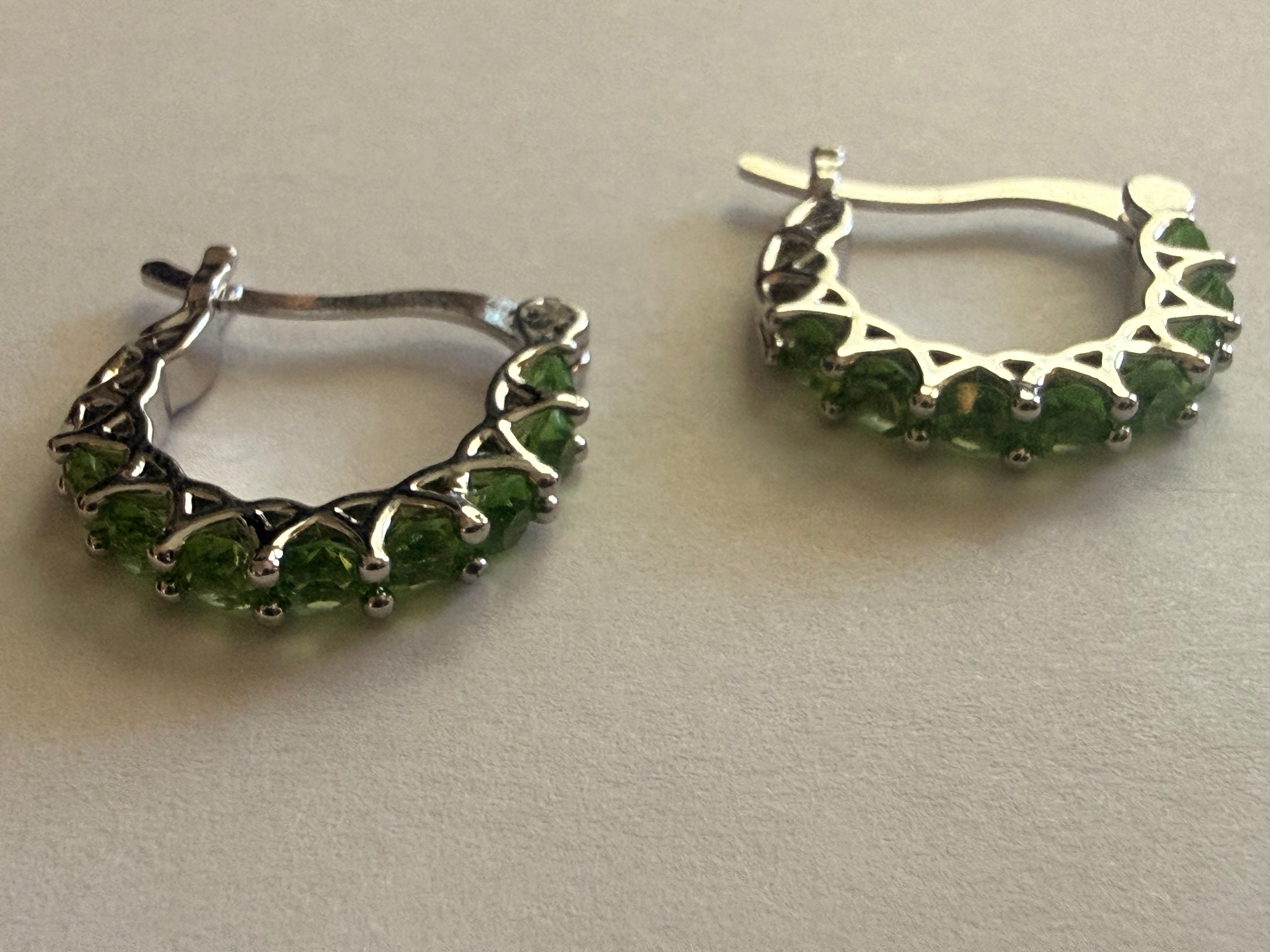 Silver-tone hoop earrings set with a row of round green rhinestones in prong settings, openwork triangular gallery, latch-back closure, both earrings