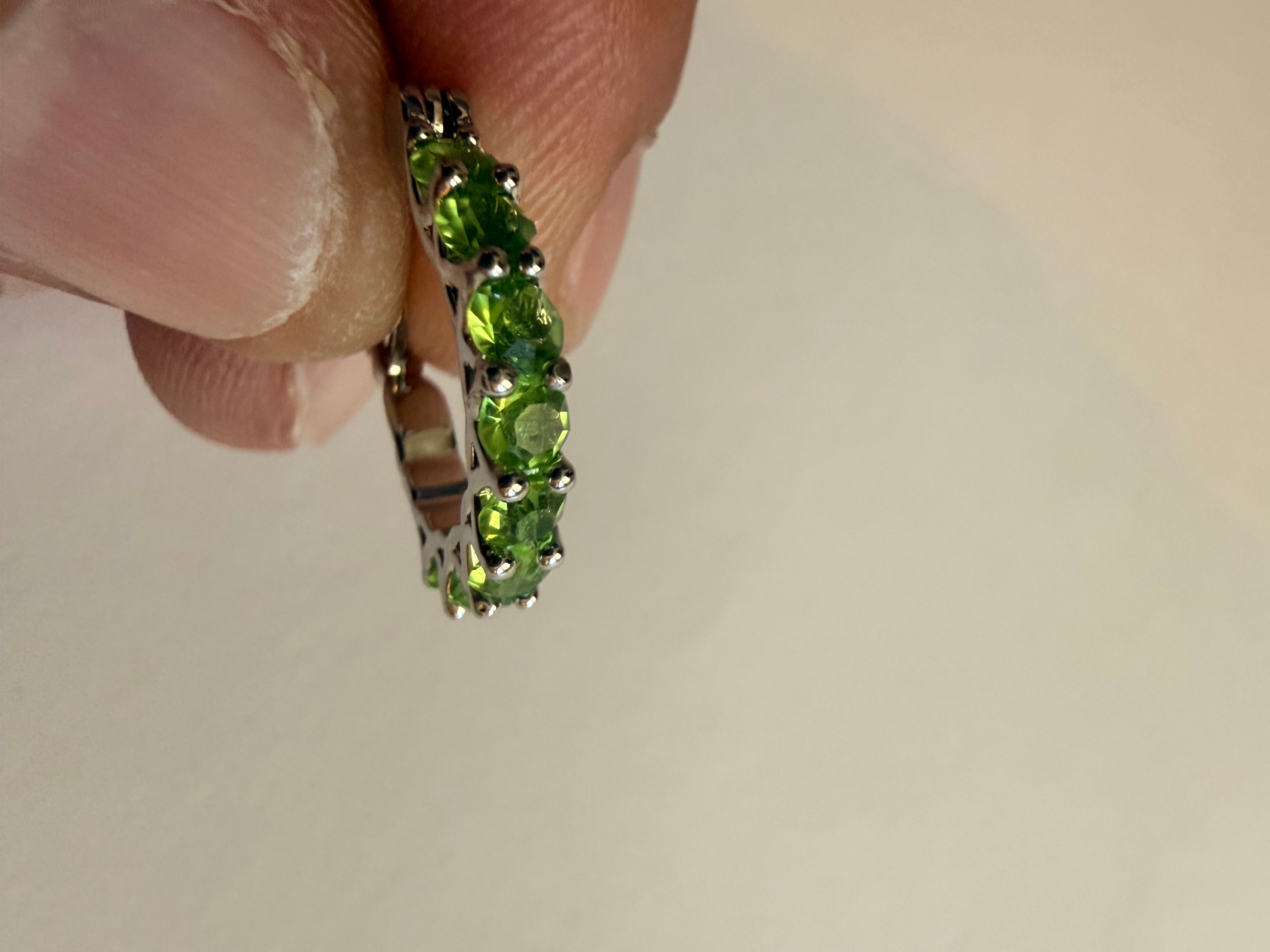 Silver-tone hoop earrings set with a row of round green rhinestones in prong settings, openwork triangular gallery, latch-back closure, edge profile showing the single row of stones