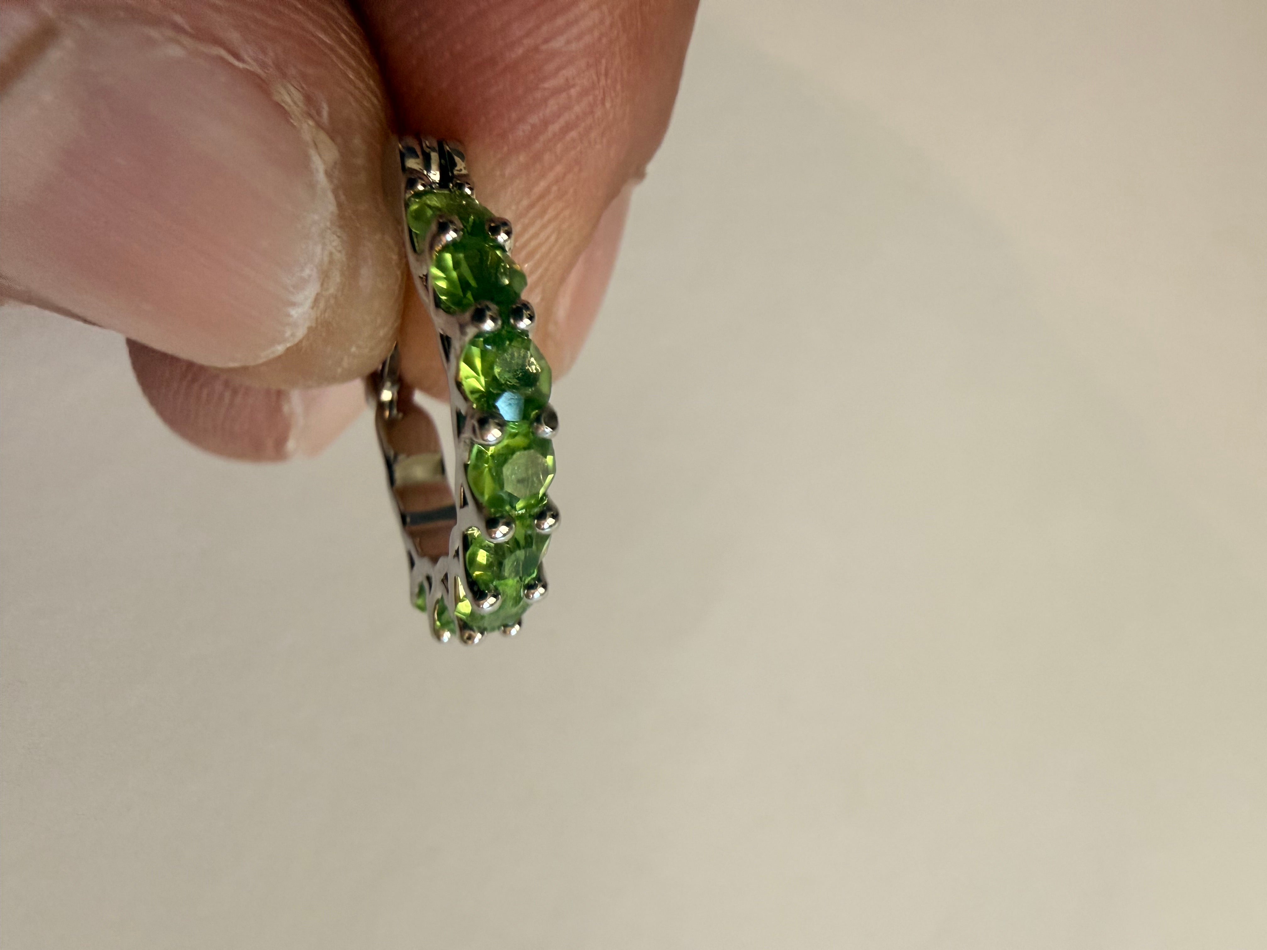 Silver-tone hoop earrings set with a row of round green rhinestones in prong settings, openwork triangular gallery, latch-back closure, edge profile and gallery