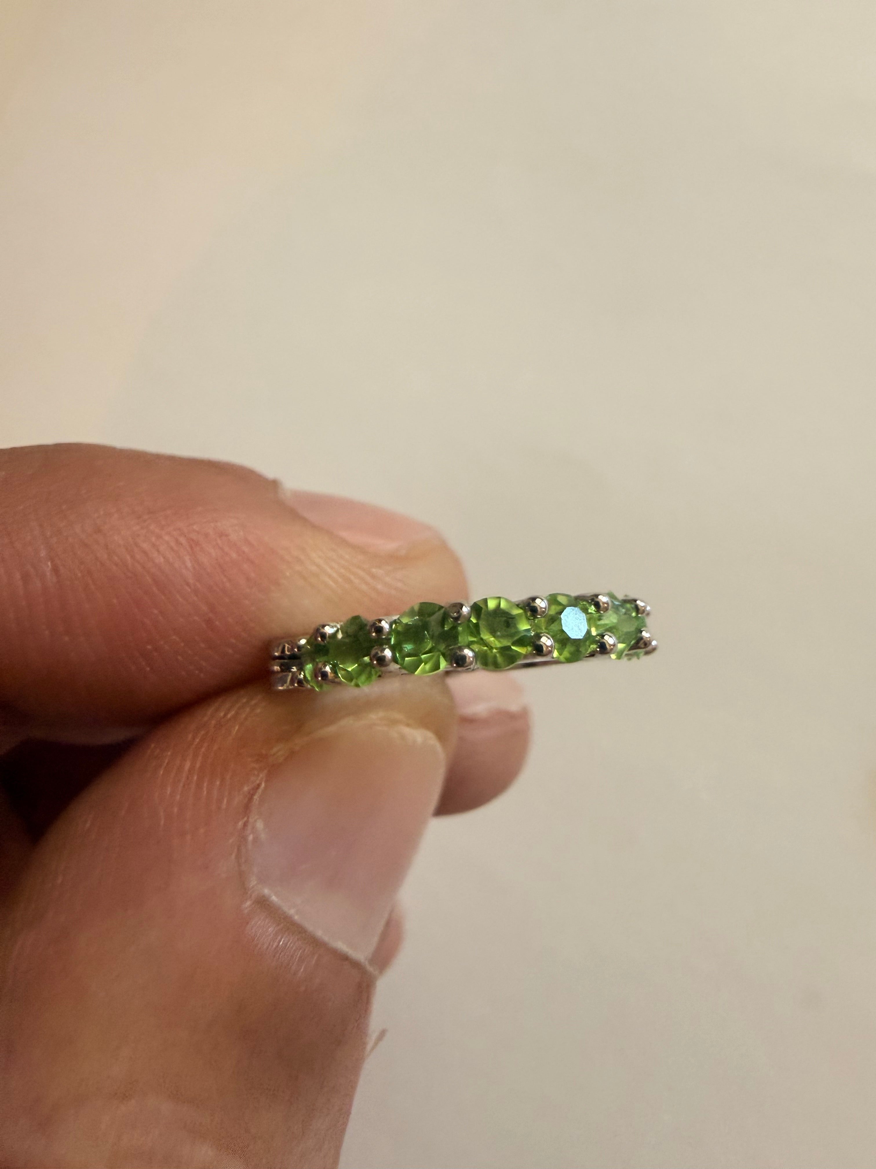 Silver-tone hoop earrings set with a row of round green rhinestones in prong settings, openwork triangular gallery, latch-back closure, held to show scale