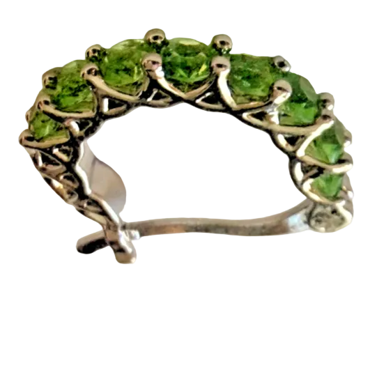 A pair of silver crescent-shaped hoop earrings set with green gemstones, displayed on a light beige surface.