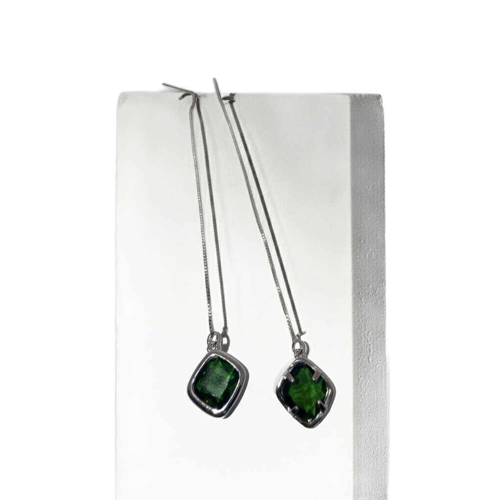 A pair of silver dangle earrings with square-cut green gemstones, hanging from a white display block against a gray background.